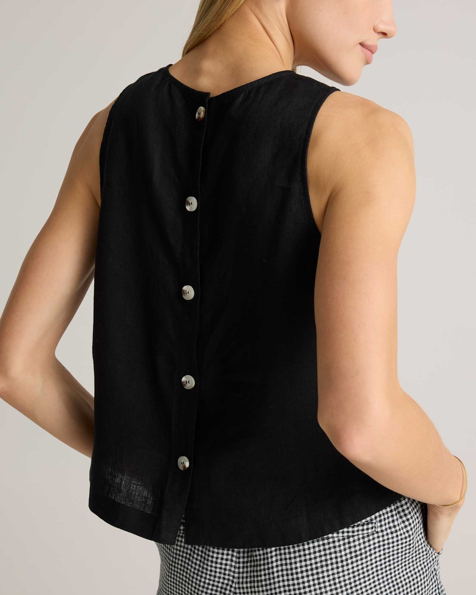A woman wears a sleeveless black top with a button-down back and checkered pants. Only her back and part of her face are visible.