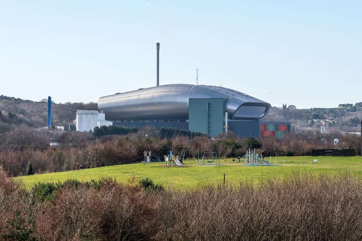 The NESS Energy from Waste facility in Aberdeen seen beyond a public park, with its distinctive curved industrial structure rising above surrounding woodland