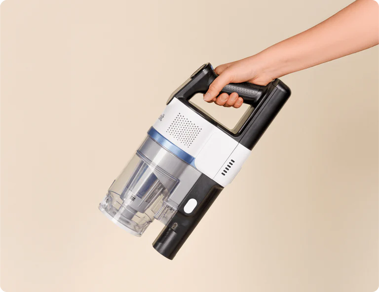 A hand holding a cordless handheld vacuum cleaner against a plain beige background.