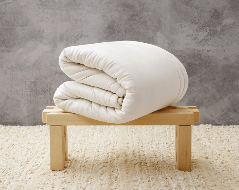 Folded white comforter placed on a small wooden bench