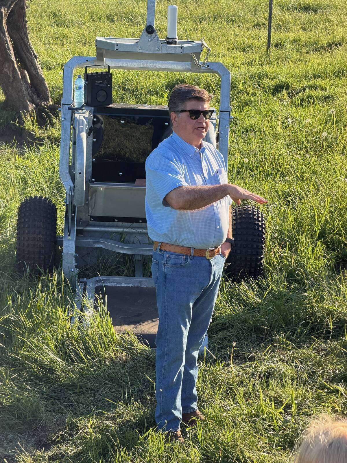 Ken Schaus gestures while speaking in front of a portable StrongBó automatic cattle scale in tall pasture grass. Photo: John Greig
