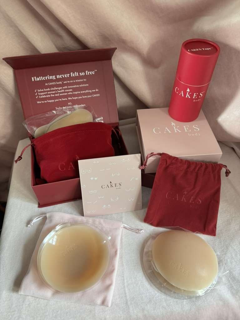Two pairs of silicone nipple covers in pouches are displayed with pink and red CAKES Body branded boxes, a card, and a cylindrical container on a white surface.