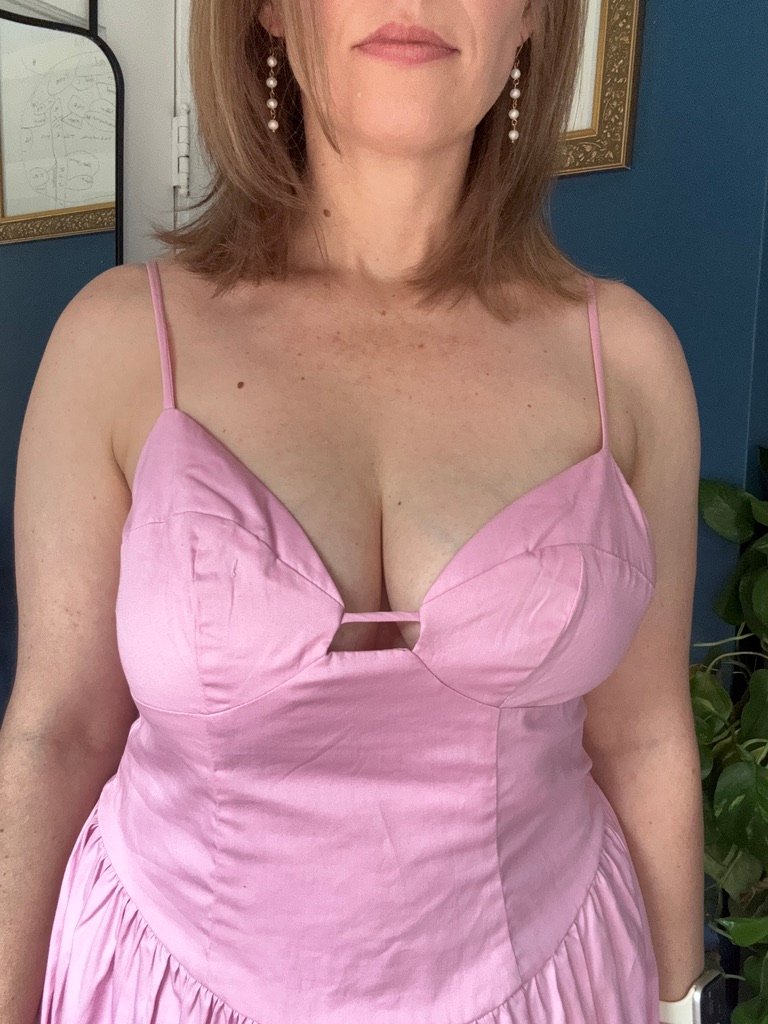 Woman in a sleeveless, light pink dress with spaghetti straps, standing indoors. The photo is cropped from shoulders to waist.