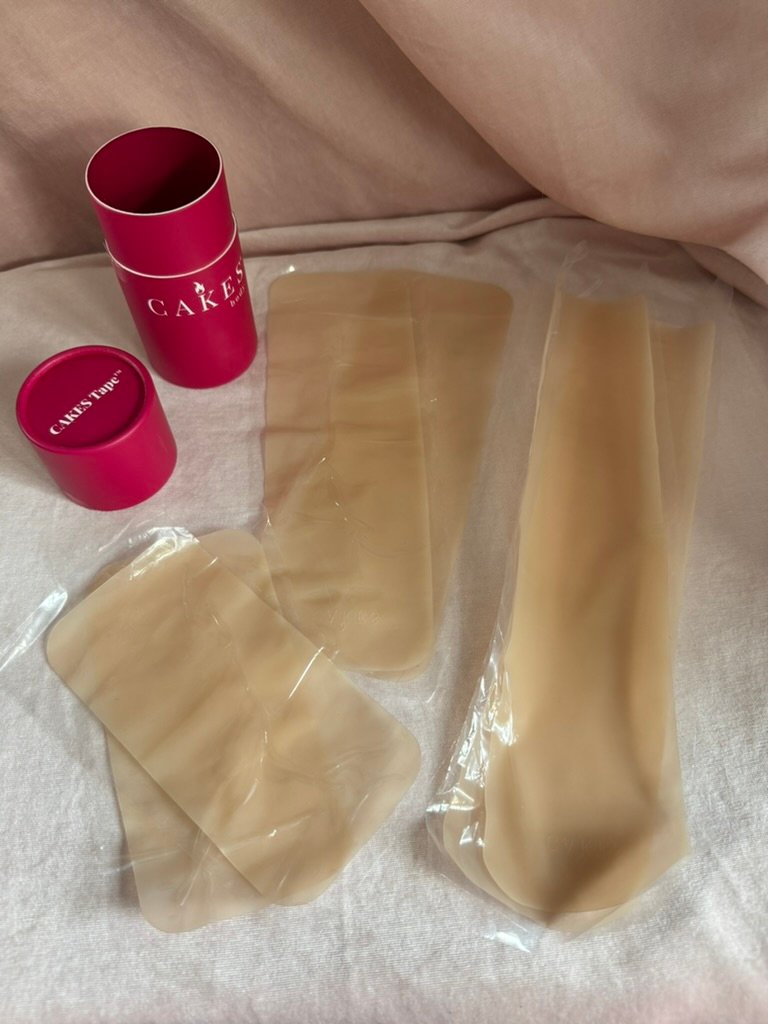 Two pink cylindrical containers labeled "CAKES" next to four beige silicone pads in clear plastic packaging on a light fabric surface.