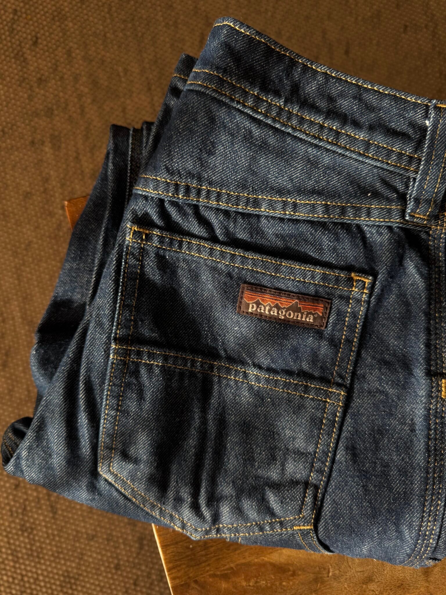 A folded pair of blue Patagonia jeans sits on a wooden surface, with the brand label visible above the back pocket.