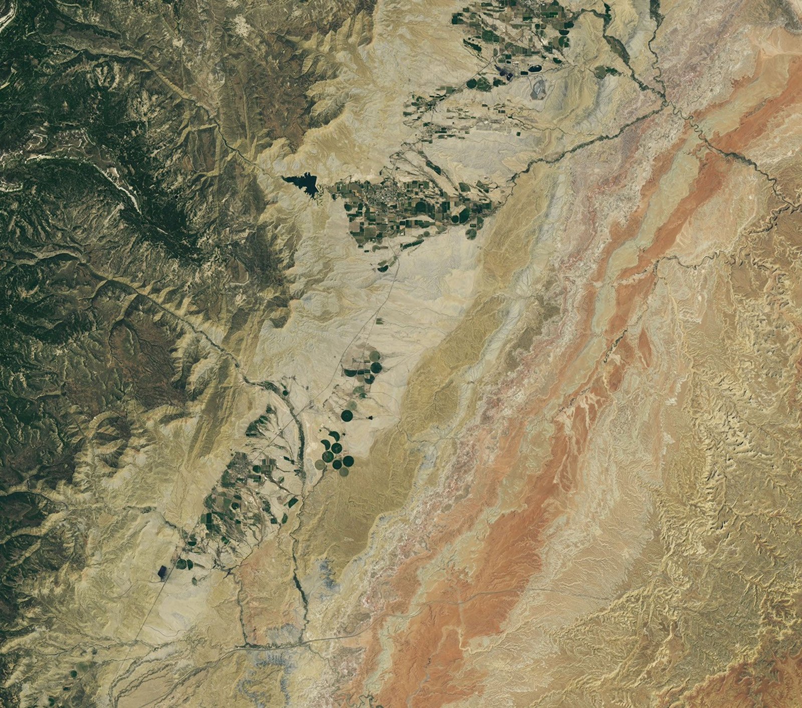 A dry, tan-colored valley containing a few circular irrigated fields runs roughly north-south through the image.