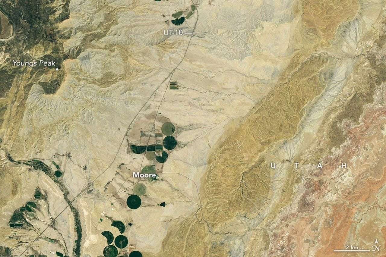 A dry, tan-colored valley containing a few circular irrigated fields runs roughly north-south through the image.
