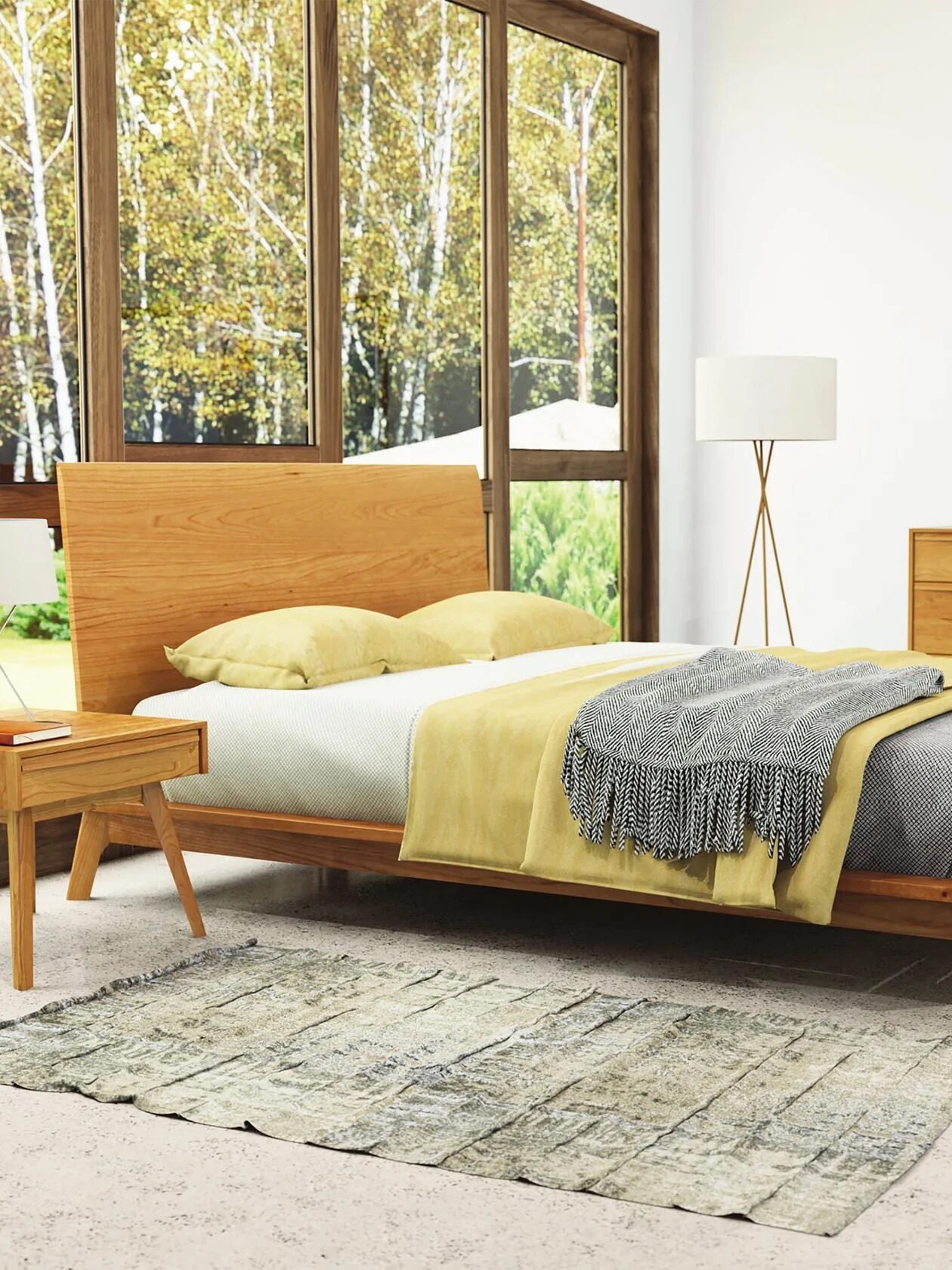 A modern bedroom with a wooden bed frame, gray and yellow bedding, a nightstand, a dresser with a mirror, a floor lamp, and large windows overlooking trees.