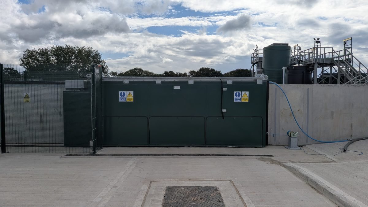 Automated sliding floodgate closed across a wastewater treatment facility entrance to create a sealed secondary containment barrier for spill protection.