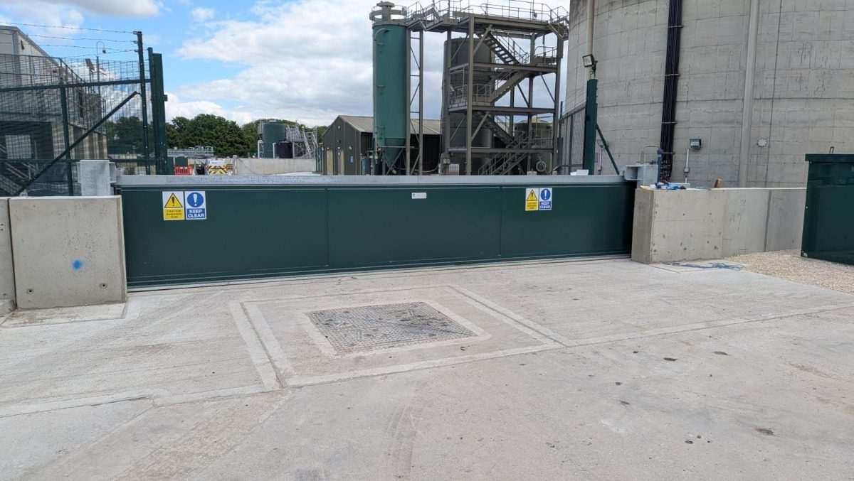 Automated sliding floodgate in the open position at a wastewater treatment facility, allowing unrestricted vehicle access while providing secondary containment capability when closed