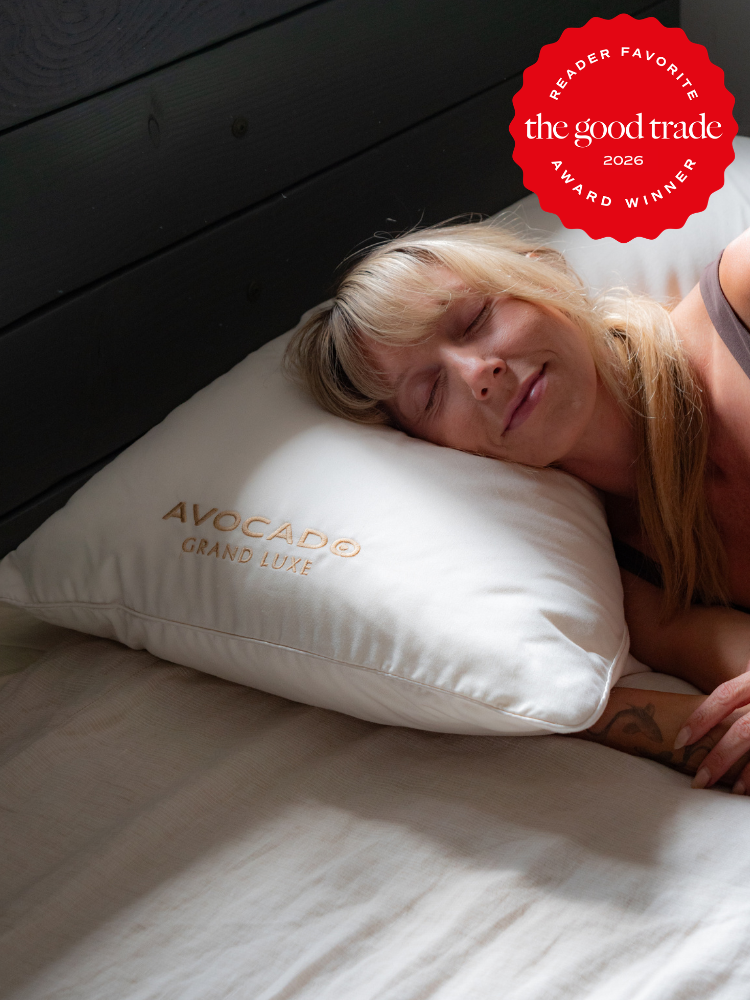 A woman peacefully sleeps on a white Avocado Grand Luxe pillow. A red badge in the corner reads "The Good Trade Reader Favorite Award Winner 2026.