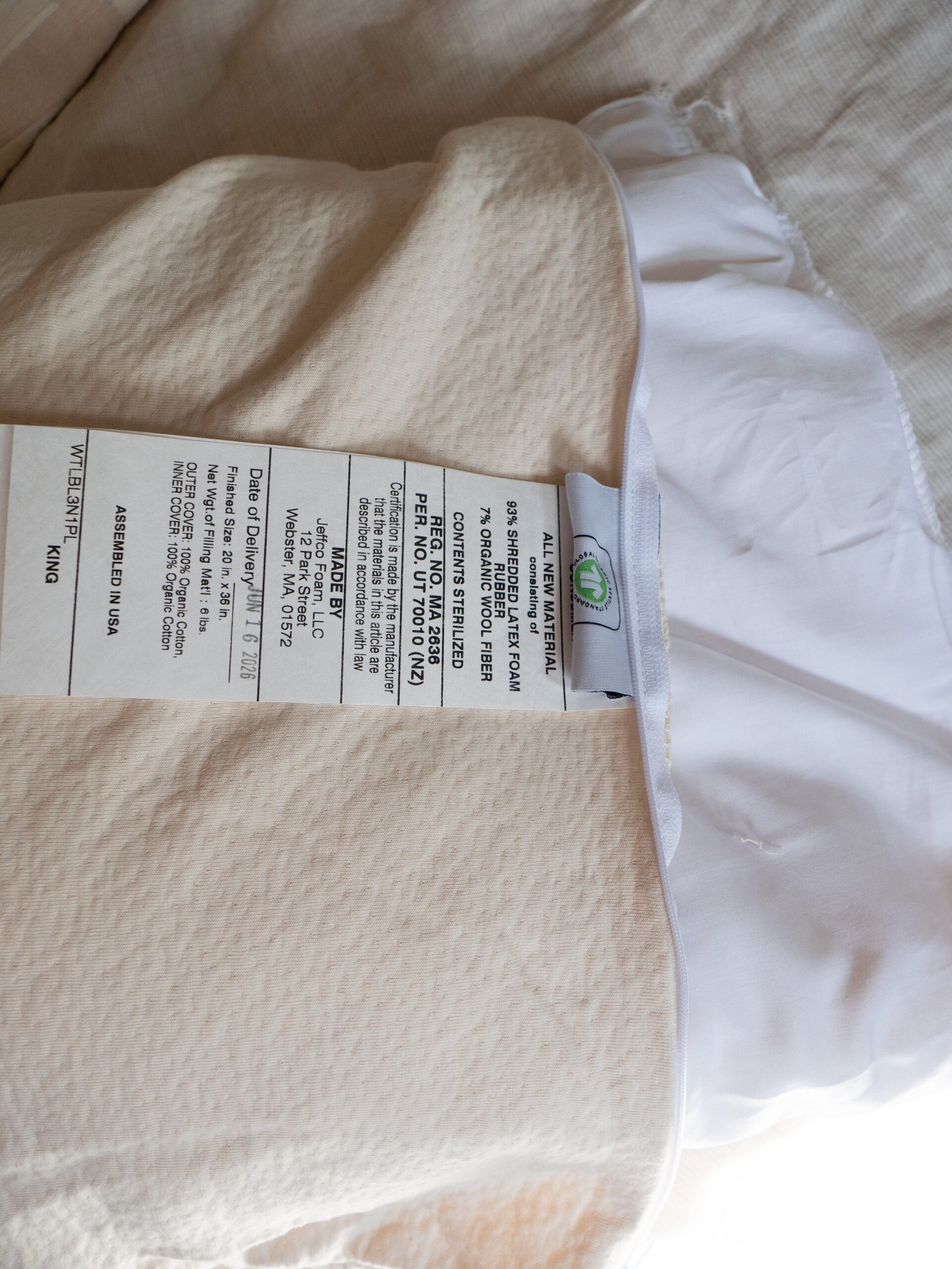 A white pillow with a visible care label listing material composition, washing instructions, and size details rests on a beige textured surface.
