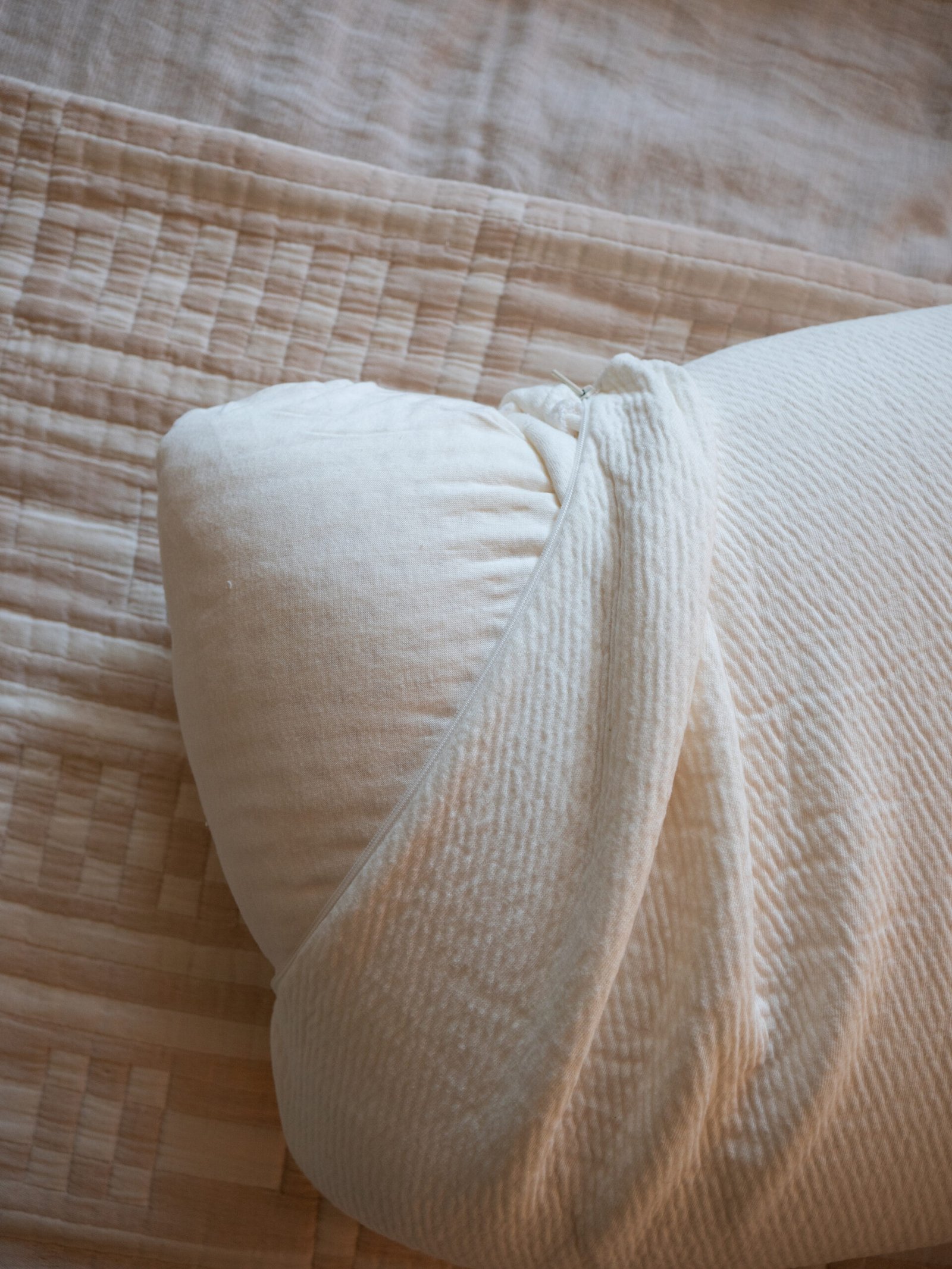 A close-up of a neatly rolled beige comforter or blanket placed on a quilted bedspread with a textured pattern.