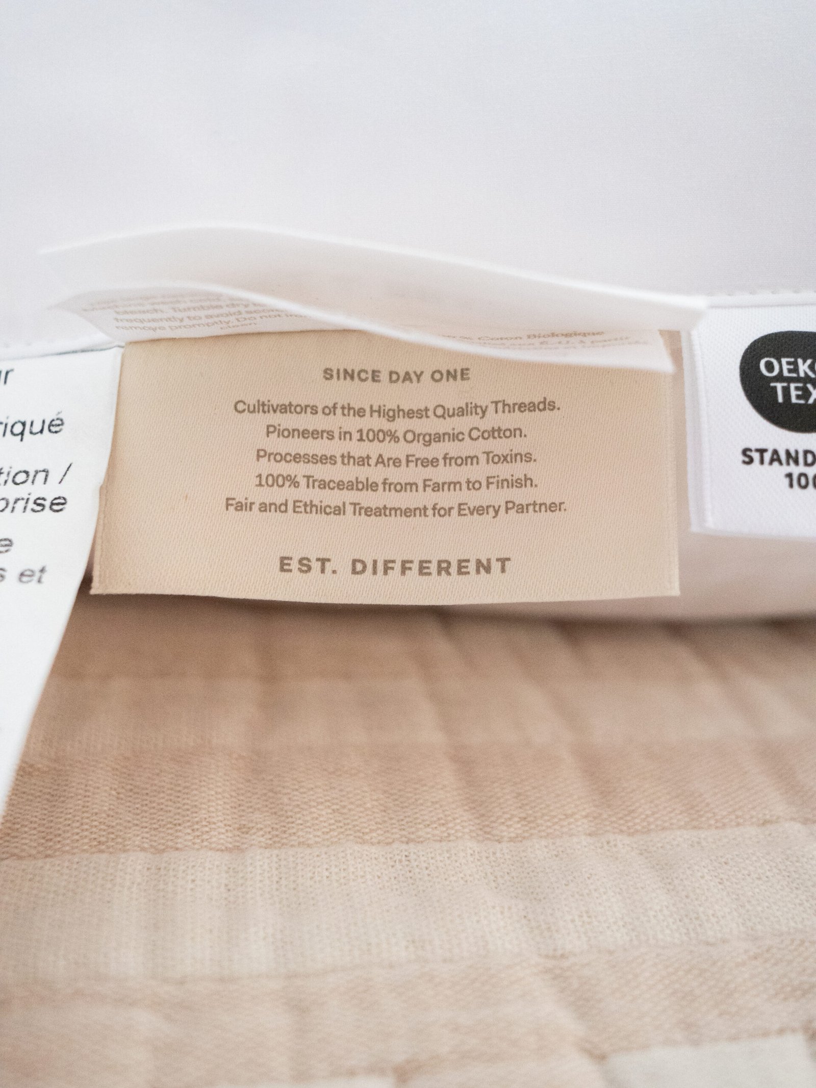 Clothing tag with text stating the use of 100% organic cotton, free from toxins, traceable from farm to finish, and ethical treatment for partners.