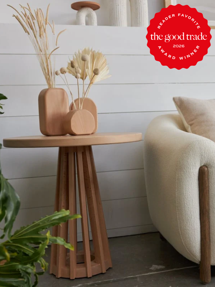 A wooden side table with geometric vases and dried plants stands next to a cream armchair; a red “The Good Trade Award Winner 2026” badge appears in the top right corner.