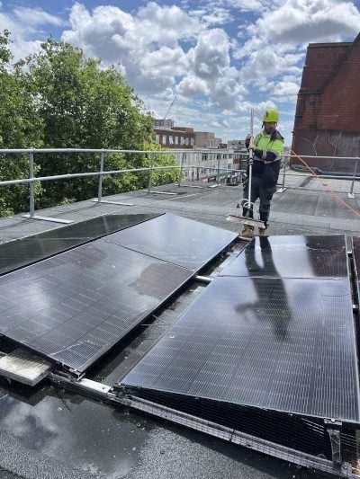 Engineer cleaning a commercial rooftop solar panel installation using a long-handled brush