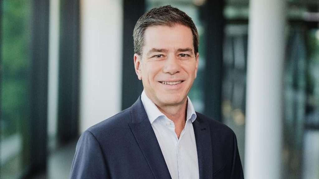 Jorge Almeida, head of sustainability for Continental's Tires sector in a profile photo. He is wearing a dark blue suit and a white shirt and is standing in an office.