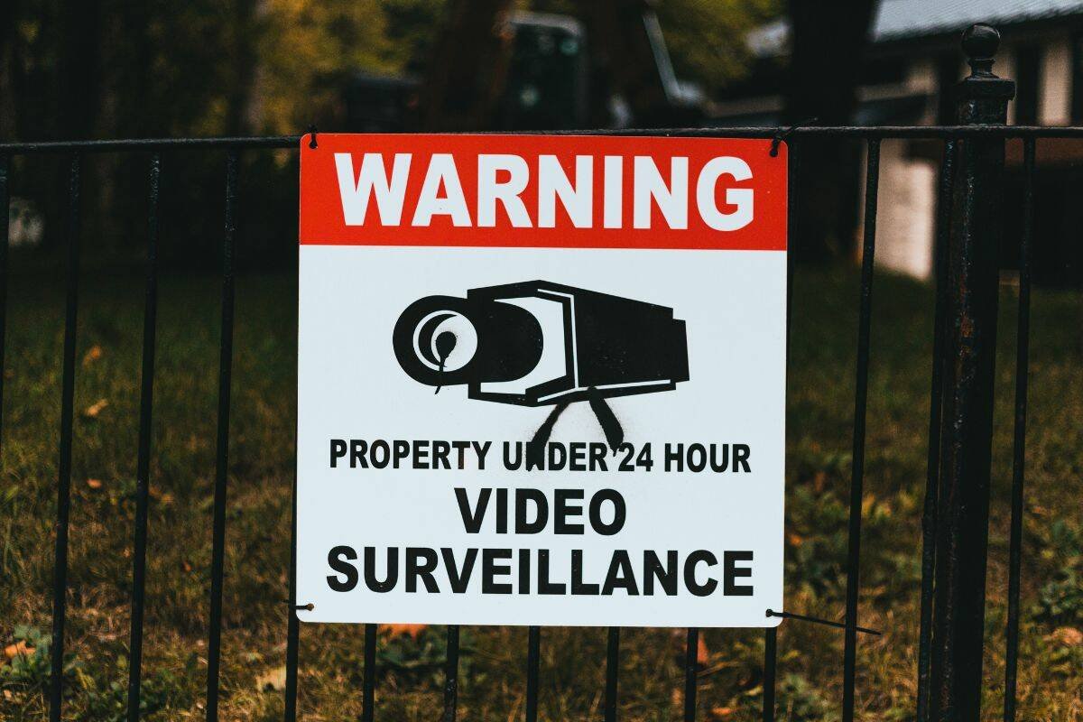 Red and white video surveillance warning sign attached to a black wrought iron fence. Photo: Erik Mclean/Pexels