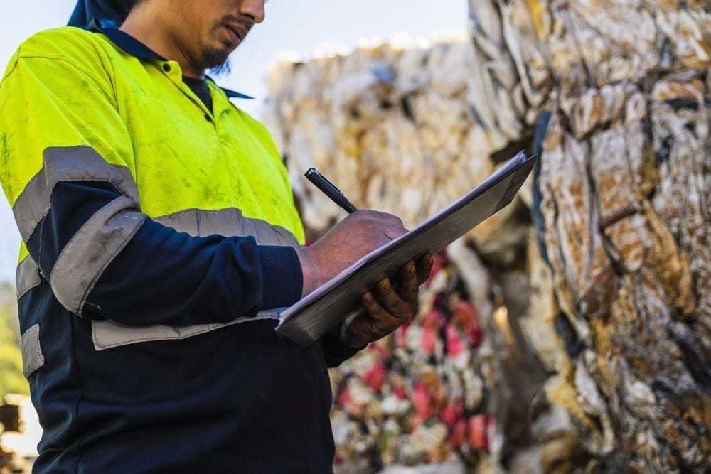 A waste management worker takes notes on his clipboard.