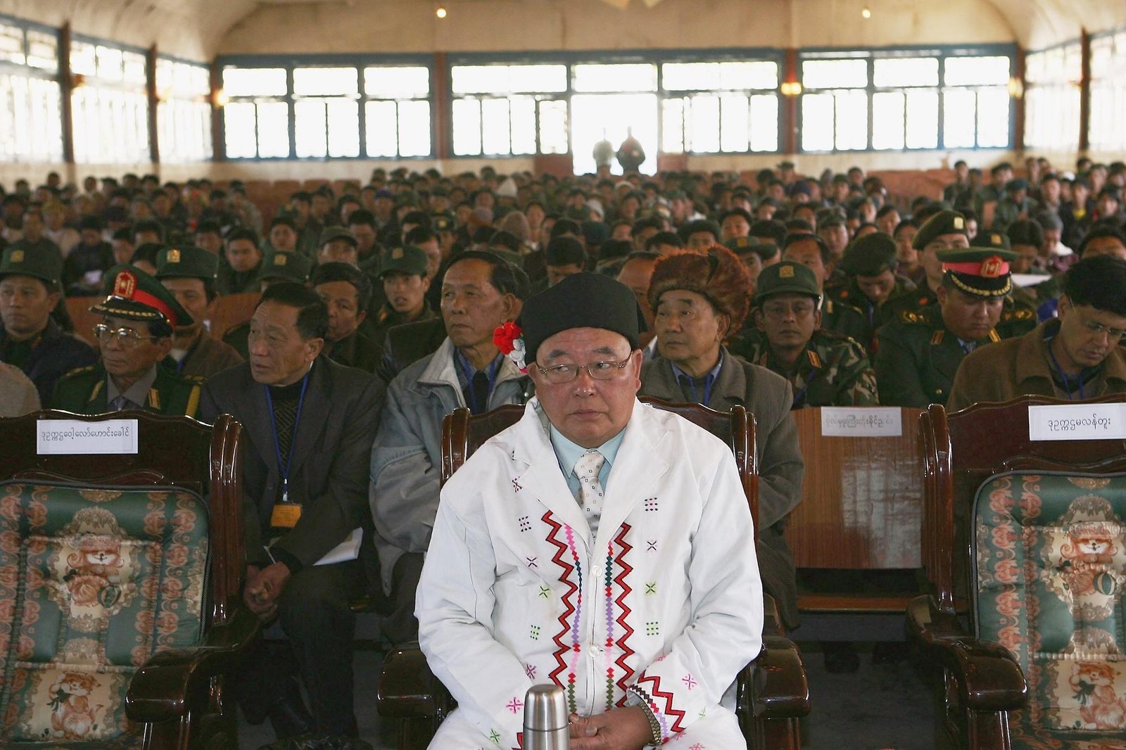 A main in ceremonial white garb sits in front of a crowd