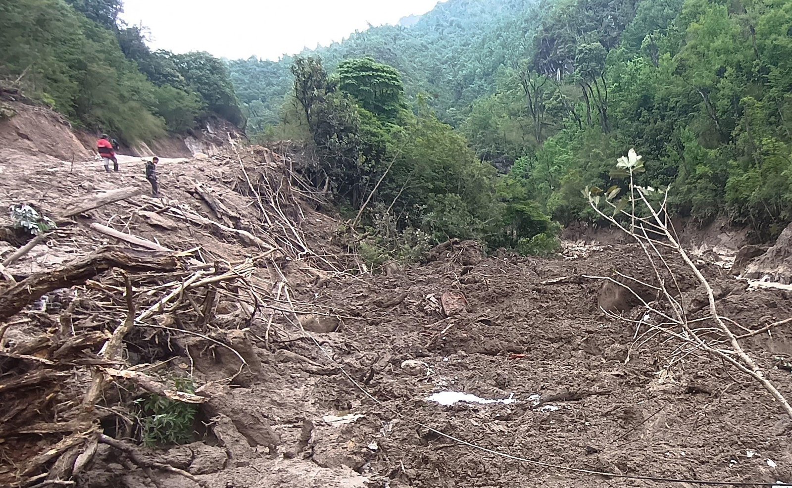 people look down at debris and dirt from a landslide