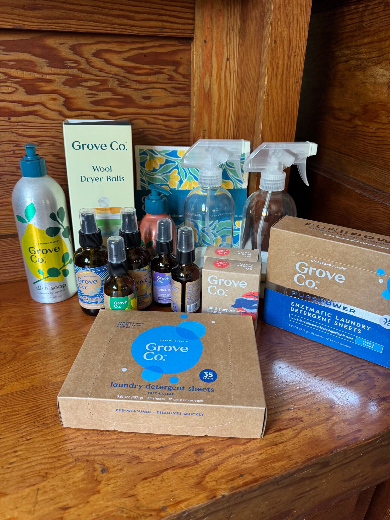 Grove Co. cleaning and household products, including detergent sheets, sprays, wool dryer balls, and essential oil bottles, arranged on a wooden surface.