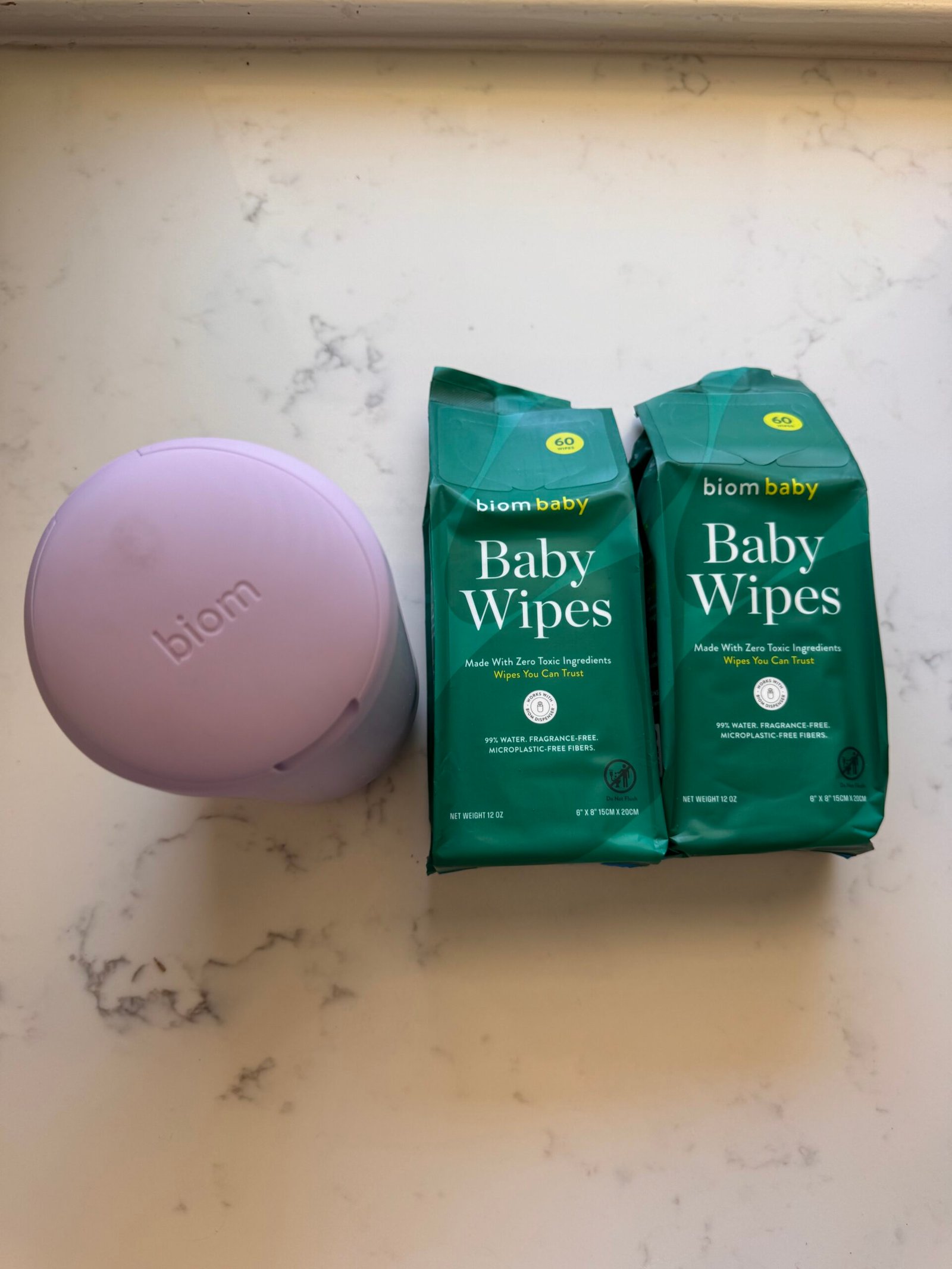 A lavender biom case and two packs of biom baby wipes are placed on a white marble surface.