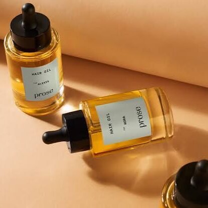 Three glass dropper bottles of Prose hair oil are arranged on a peach-colored surface, with one bottle lying down and two standing upright—perfect for stocking up during the July sales.