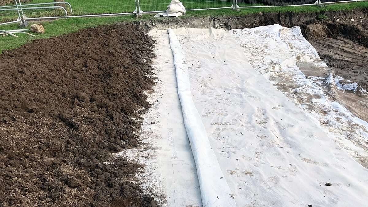 A geocomposite waterproof liner being installed in a large excavated sustainable drainage (SuDS) basin, with earth backfill alongside, as part of the Derringham Aqua Greens flood resilience project in Hull