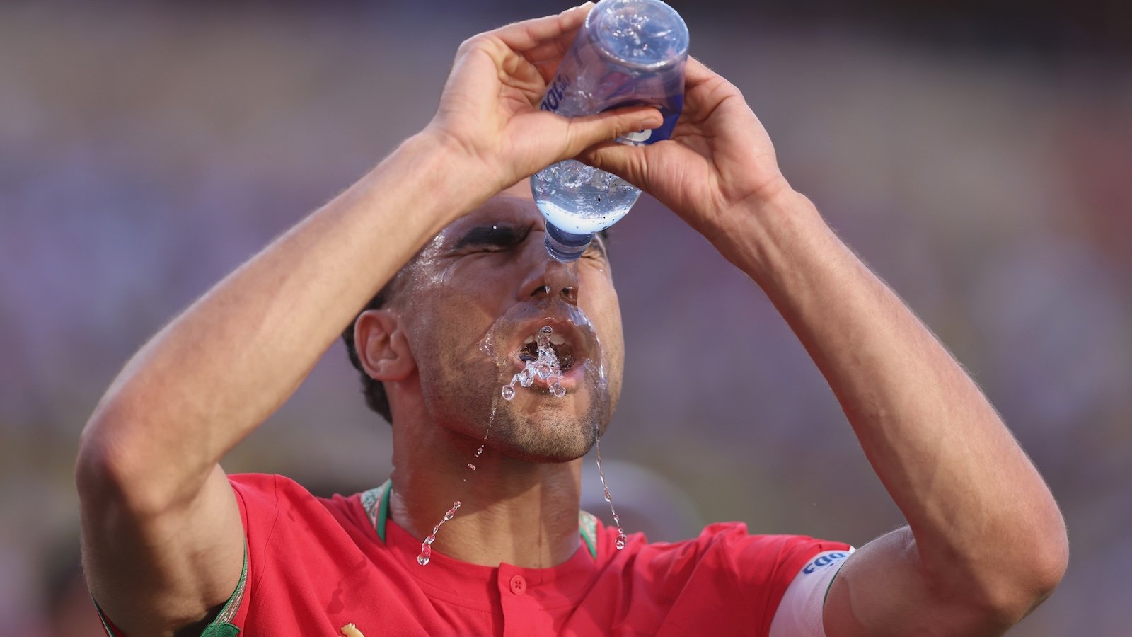 A soccer player douses his face with the bottle of water during a World Cup match.