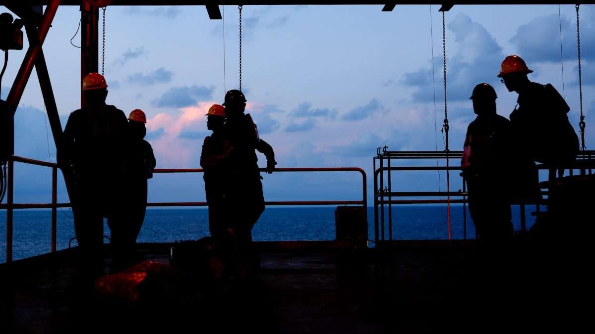 Silhouetted offshore workers wearing safety helmets on a marine platform at sea during dusk
