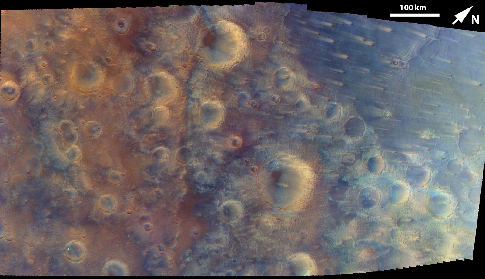 An overhead satellite mosaic of the Martian surface, showing numerous impact craters in a transition zone of reddish-brown and dusty blue terrain, with streaks stretching across the blue region.