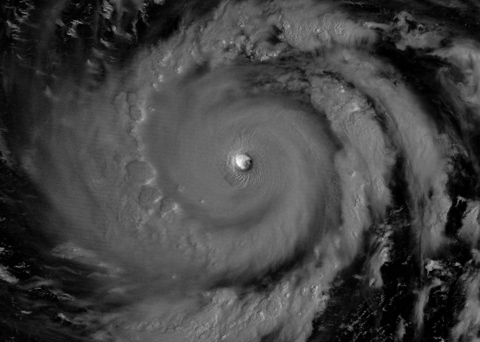 The eyewall of a super typhoon is partially illuminated by moonlight in a nighttime satellite image.