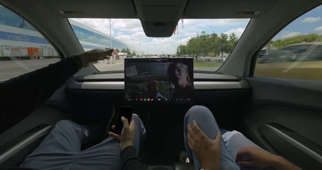 tesla cybercab with no manual controls showing a movie with two employees inside