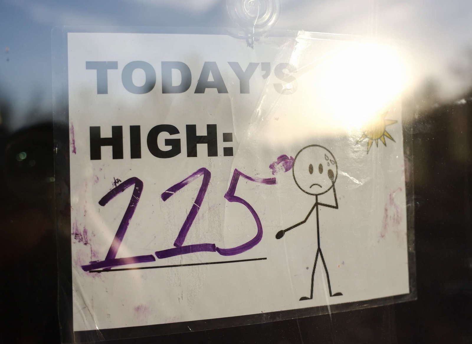 A sign posted in a window reads Today's High 115 with a frowning stick figure