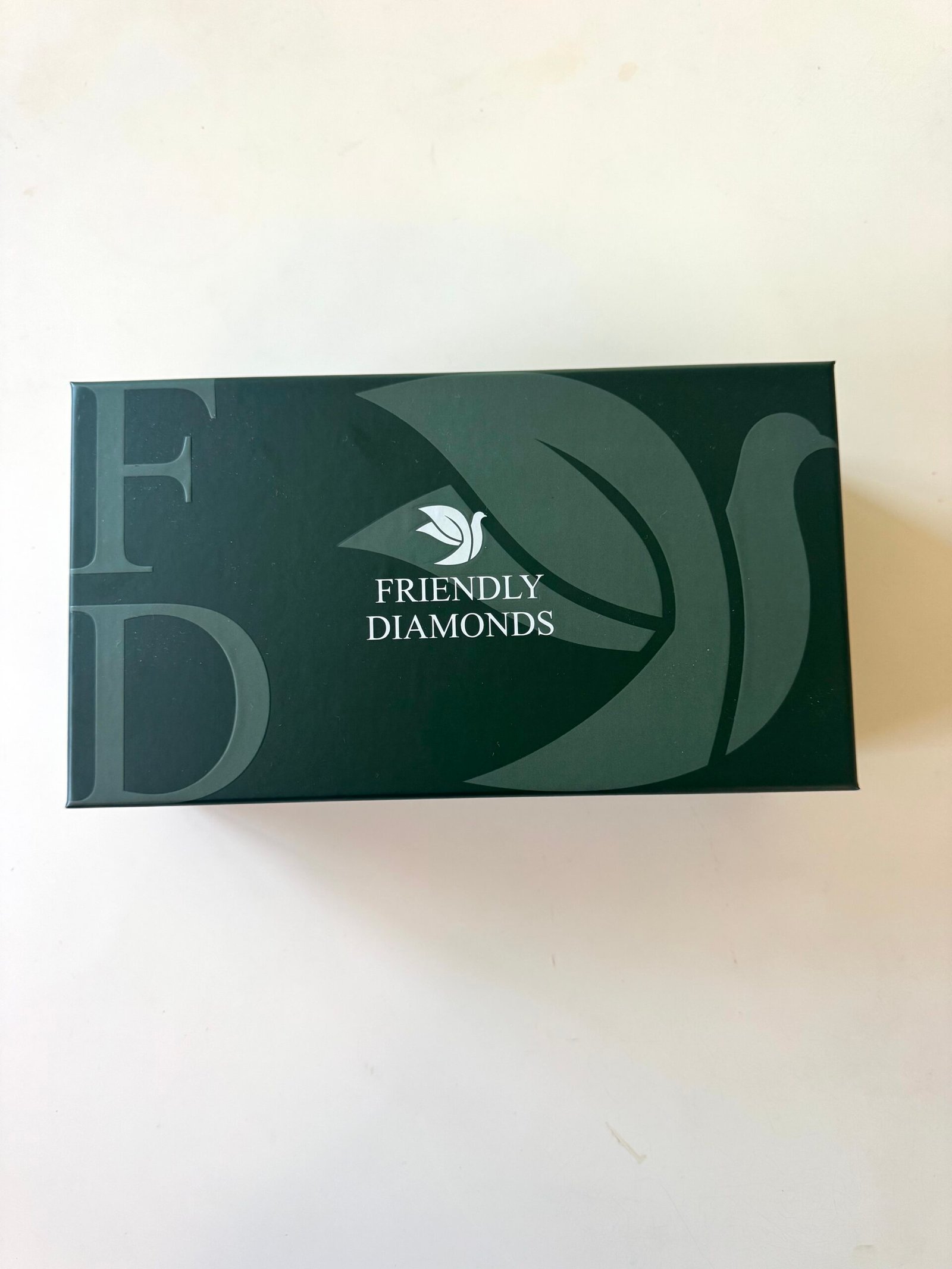 A dark green rectangular box with "FRIENDLY DIAMONDS" and a bird logo printed on the top, along with large letters "F" and "D" in the background.