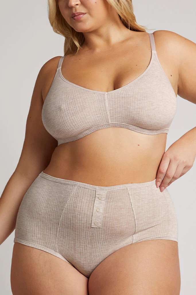 A woman wearing a beige ribbed bra and high-waisted underwear with button details poses against a plain background.