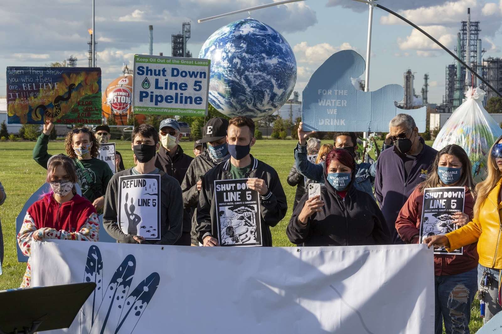 Protesters stand with signs saying Shut Down Line 5 Pipeline and For the Water We Drink