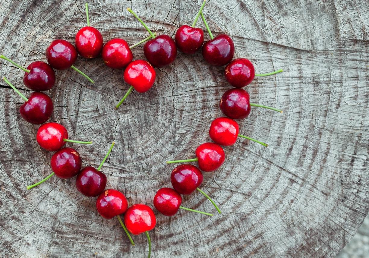 Cherries in the shape of a heart on wooden background