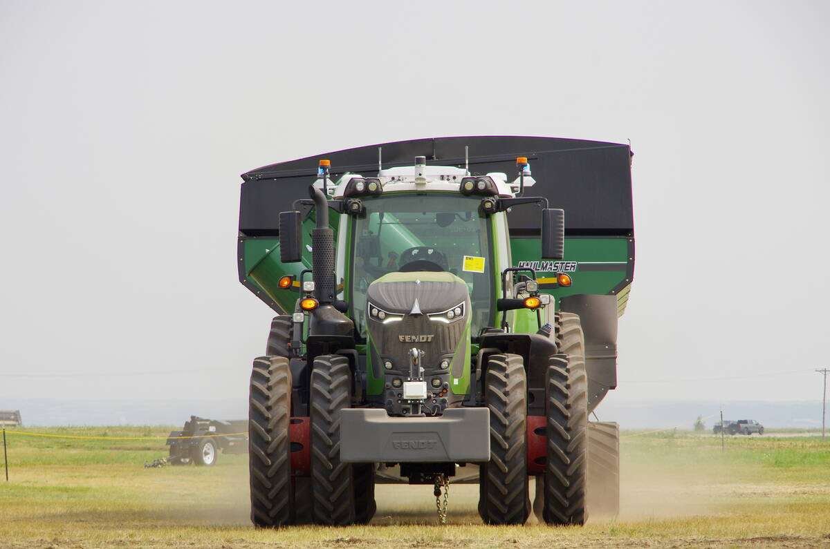 A green Fendt tractor fitted with roof-mounted autonomy sensors and beacons pulls a grain cart across a field, viewed head-on. Photo: Alexis Stockford