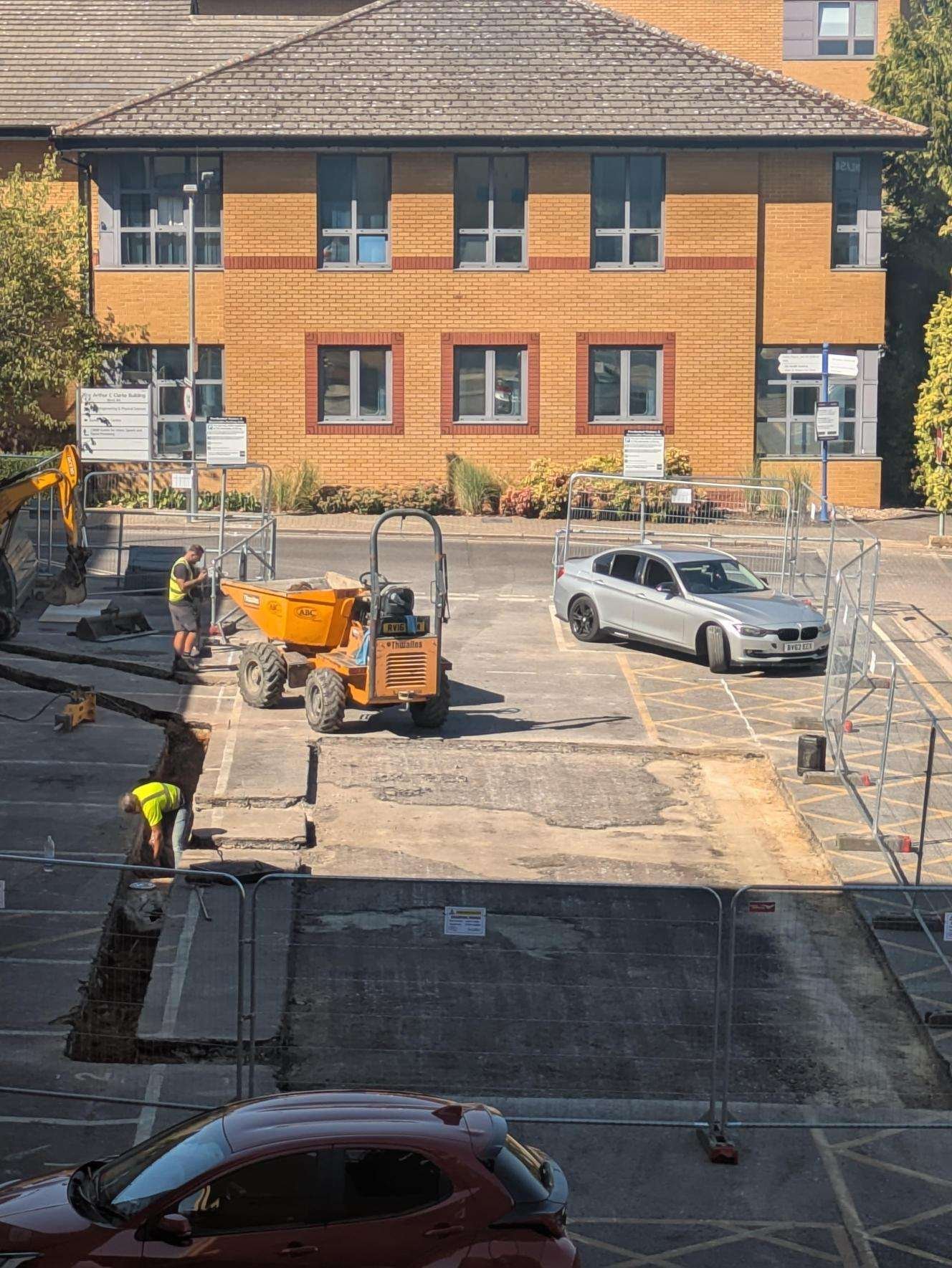 Construction workers and machinery carrying out roadworks in a car park outside a brick building