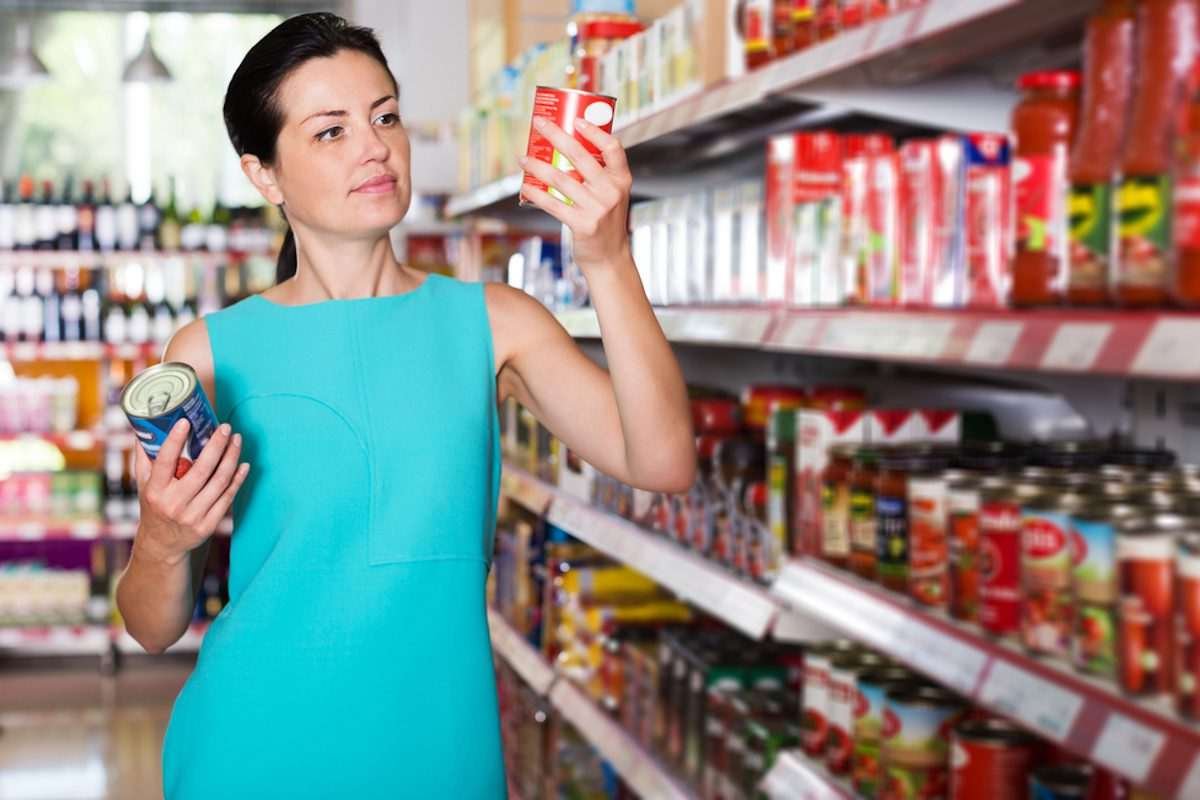 Woman checking the labelling on a package lifted off the supermarket shelf