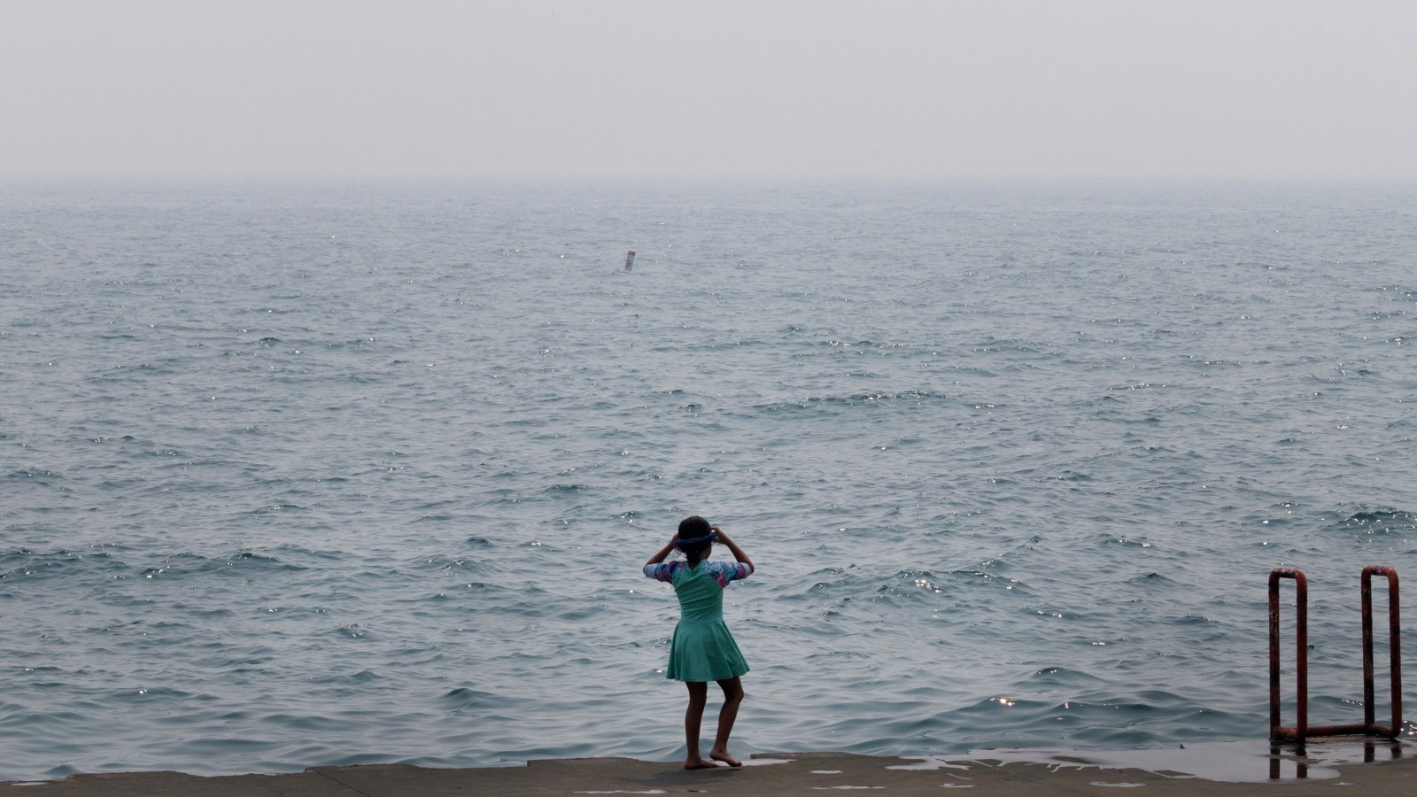 A child stands in front of a murky sea
