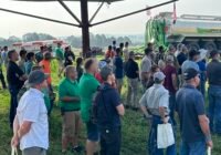 A crowd watches a liquid manure demonstration under a tent in a field.