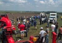 A crowd gathers at a liquid manure pit, with machinery nearby.