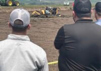 Two men watch a manure boat in a pit of liquid manure.