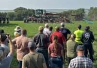 A crowd watches a liquid manure demonstration in a field.