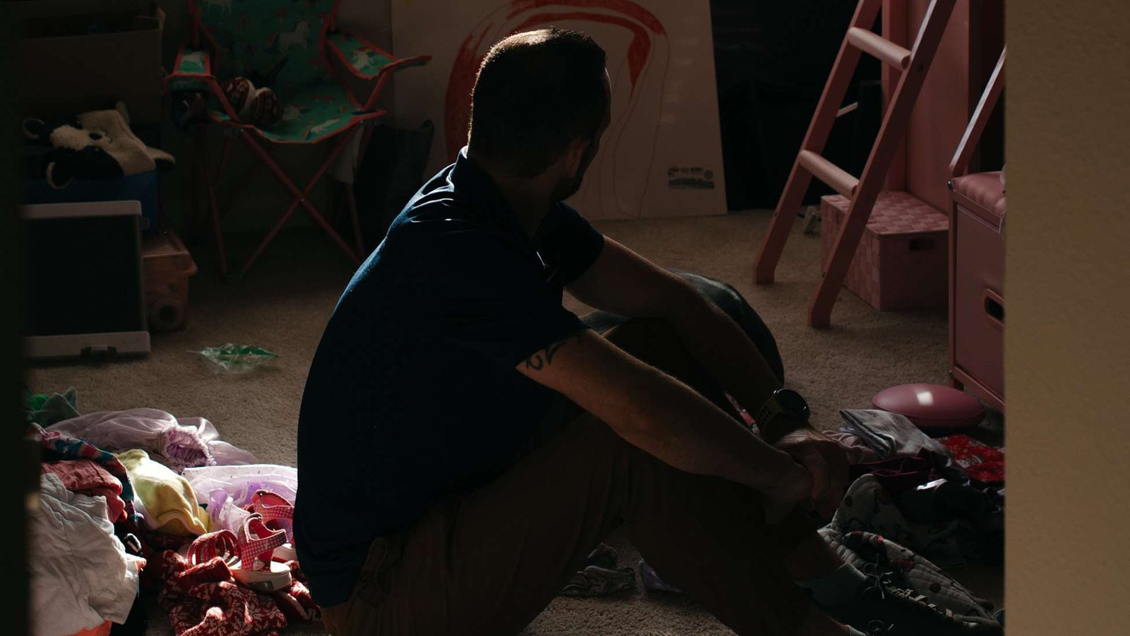 A man's face is obscured as he sits in a child's room looking away from the camera