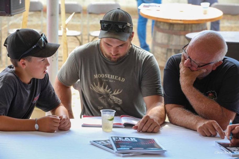 A boy, a young man and an older man study a Peak Performance sale catalogue at a table. Photo: courtesy Mount Elgin Dairy Farms
