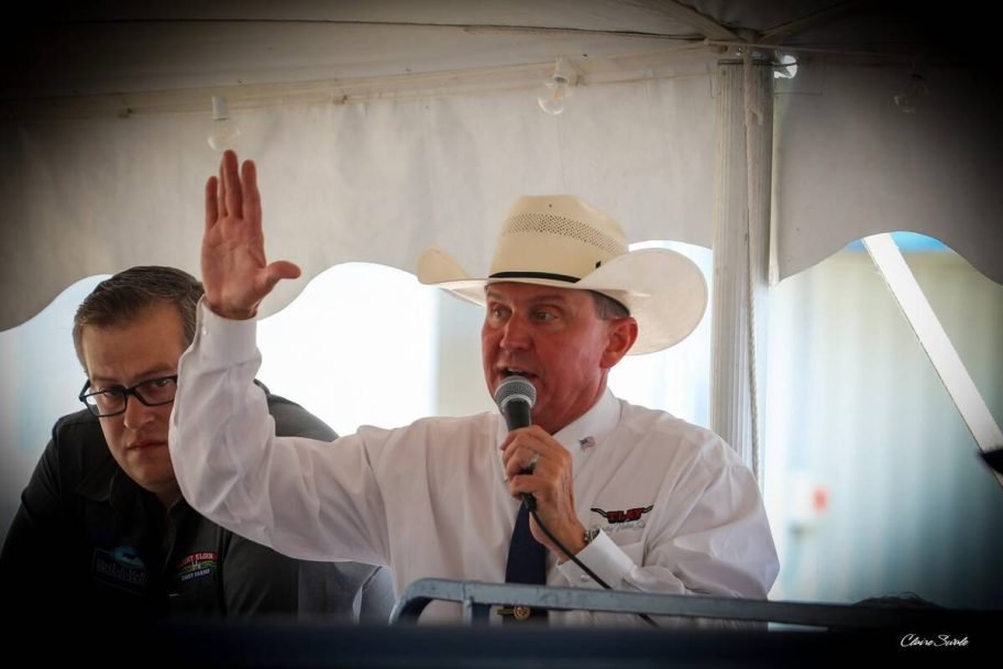 An auctioneer in a white cowboy hat raises a hand while speaking into a microphone from the block. Photo: courtesy Mount Elgin Dairy Farms
